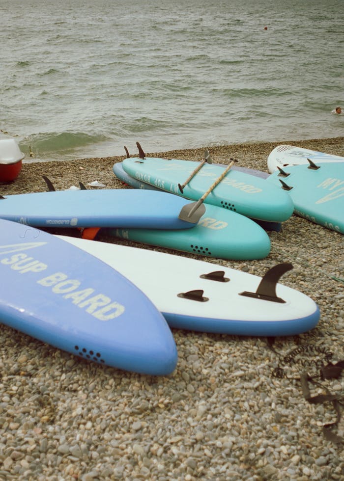 Bright surfboards rest on a pebble beach by the sea, ready for adventure.