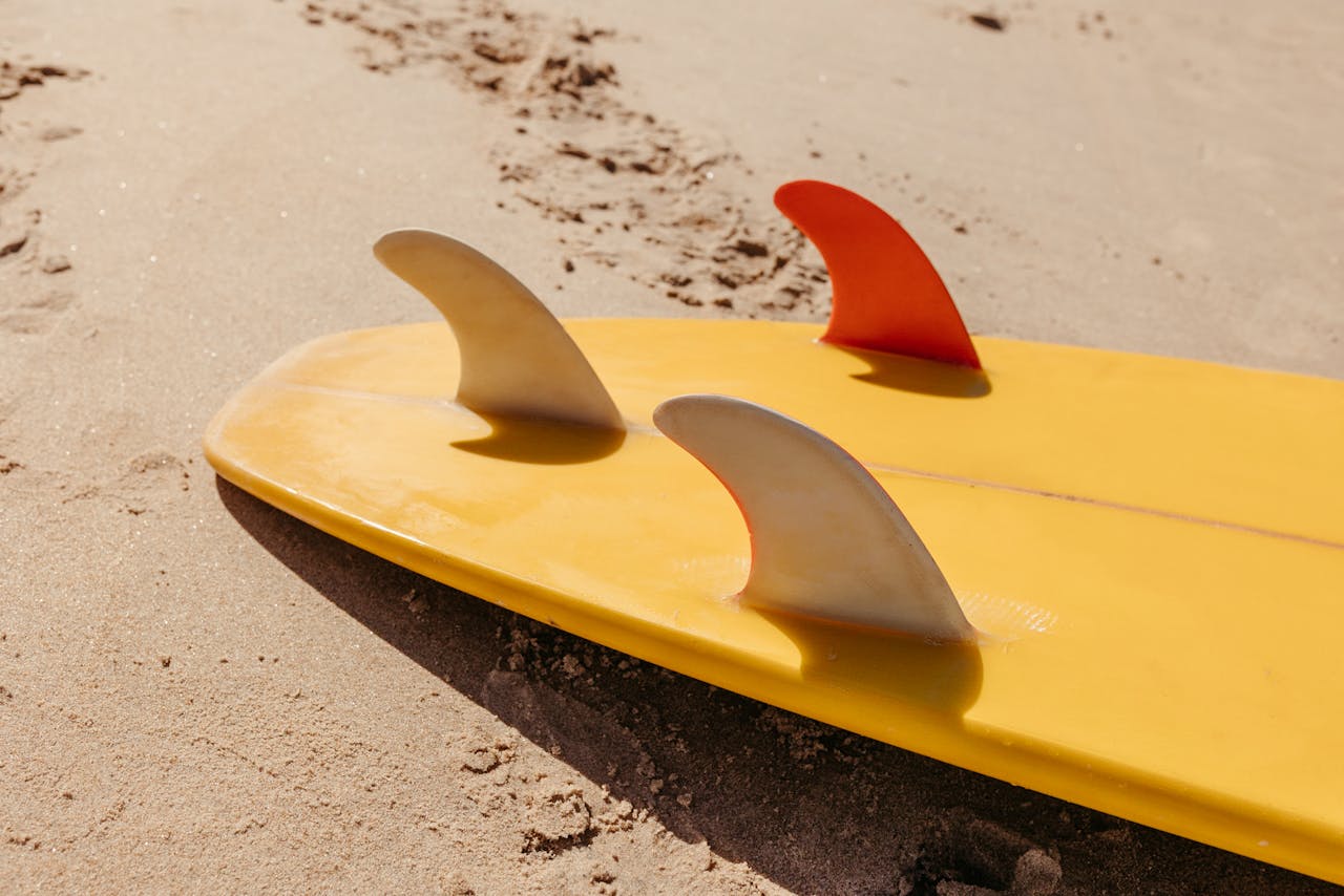 Yellow surfboard with colorful fins resting on sandy beach ready for adventure.