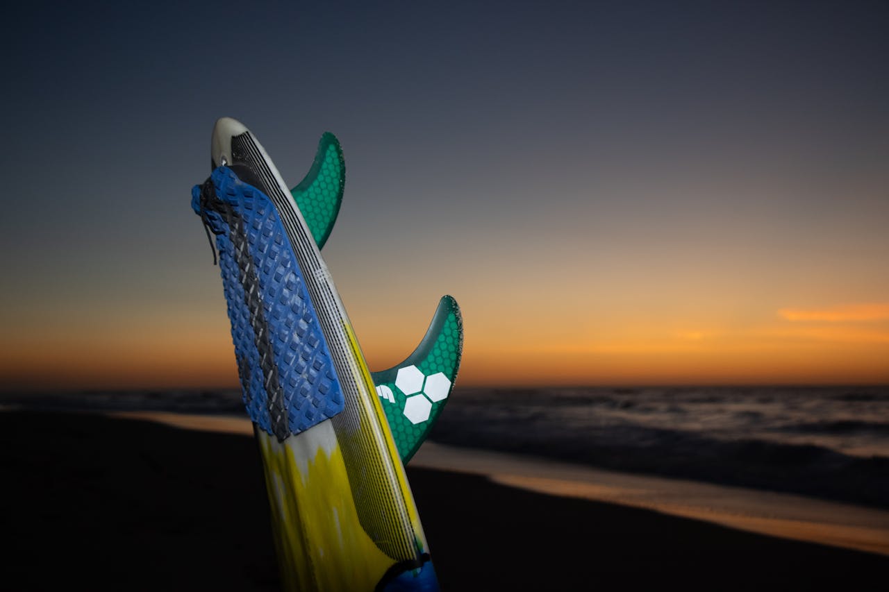 Surfboard standing on beach during a vibrant sunset by the ocean surf.