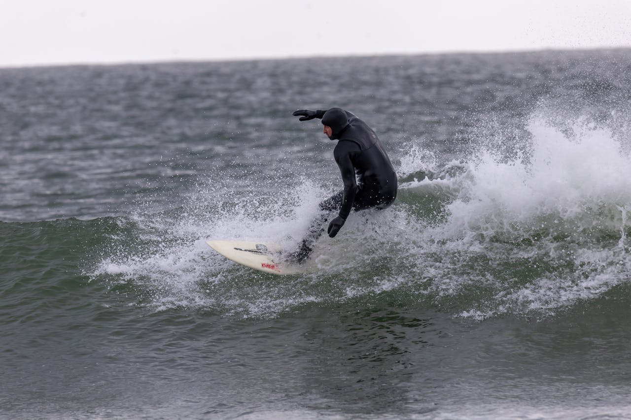 Surfer navigating a wave in dynamic motion, clad in black wetsuit. Ocean adventure at daytime.